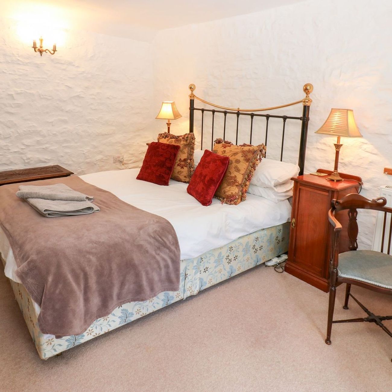 The king-size bedroom at Farrier's Cottage, with a brass and iron bedstead against a whitewashed stone wall, lamps lit on either side