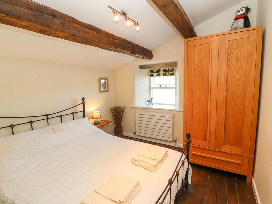 A bedroom with a bed a wooden wardrobe a window and exposed wooden beams at Roger Pot in Garsdale near Sedbergh