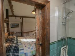 A bedroom with a bed and chair visible through a wooden door next to a shower area with green and white tiles at The Old Cart House in Garsdale near Sedbergh