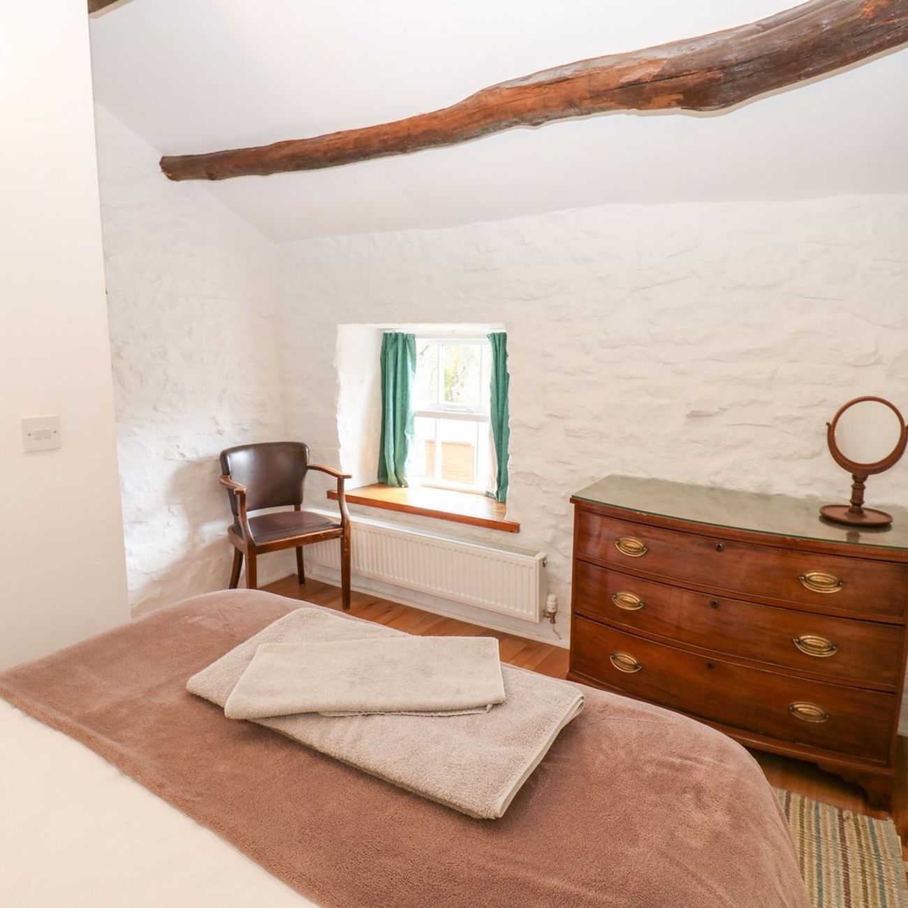 A bedroom at Farrier's Cottage with an exposed roof beam overhead, an antique chest of drawers and towels laid out on the bed