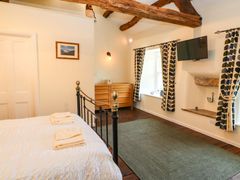 A bedroom with a bed with folded towels on it a wooden dresser a wall-mounted TV and curtains on windows at Roger Pot in Garsdale near Sedbergh
