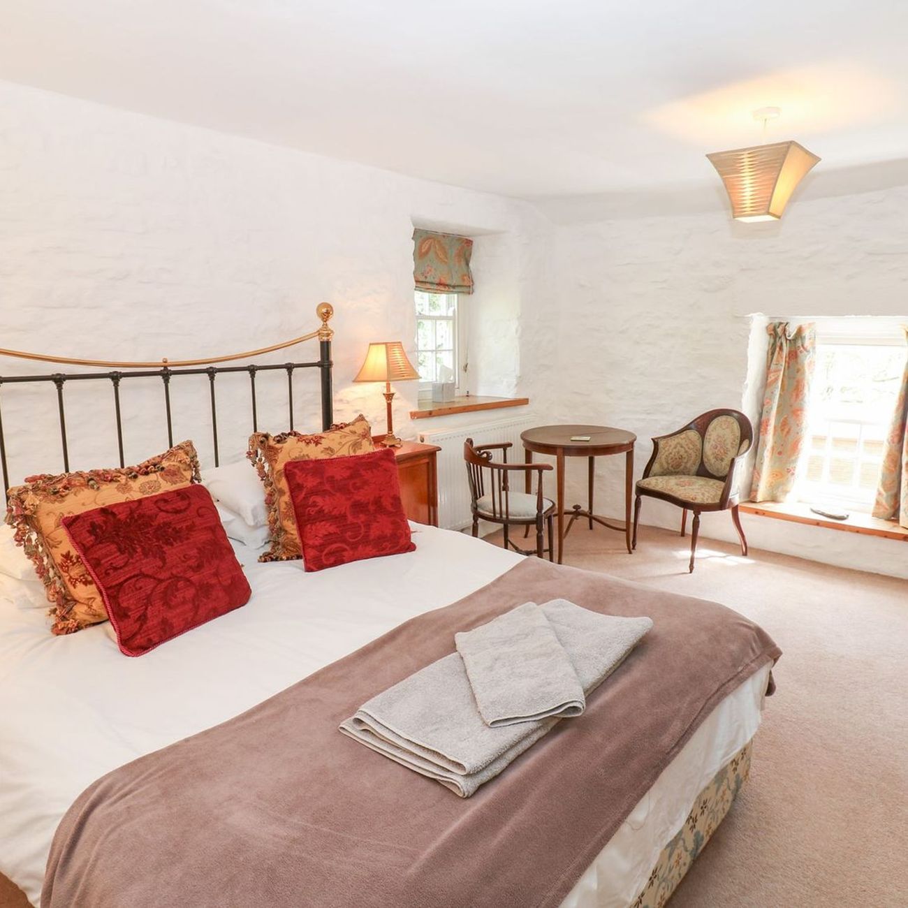 The king-size bedroom at Farrier's Cottage, with whitewashed stone walls, a small table and two antique chairs beside the window