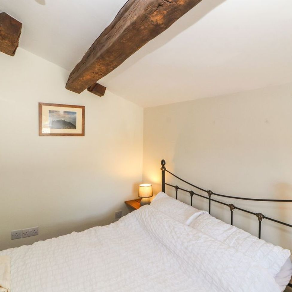 A bedroom with a metal bed frame white bedding wooden ceiling beams and a small bedside lamp at Roger Pot in Garsdale near Sedbergh