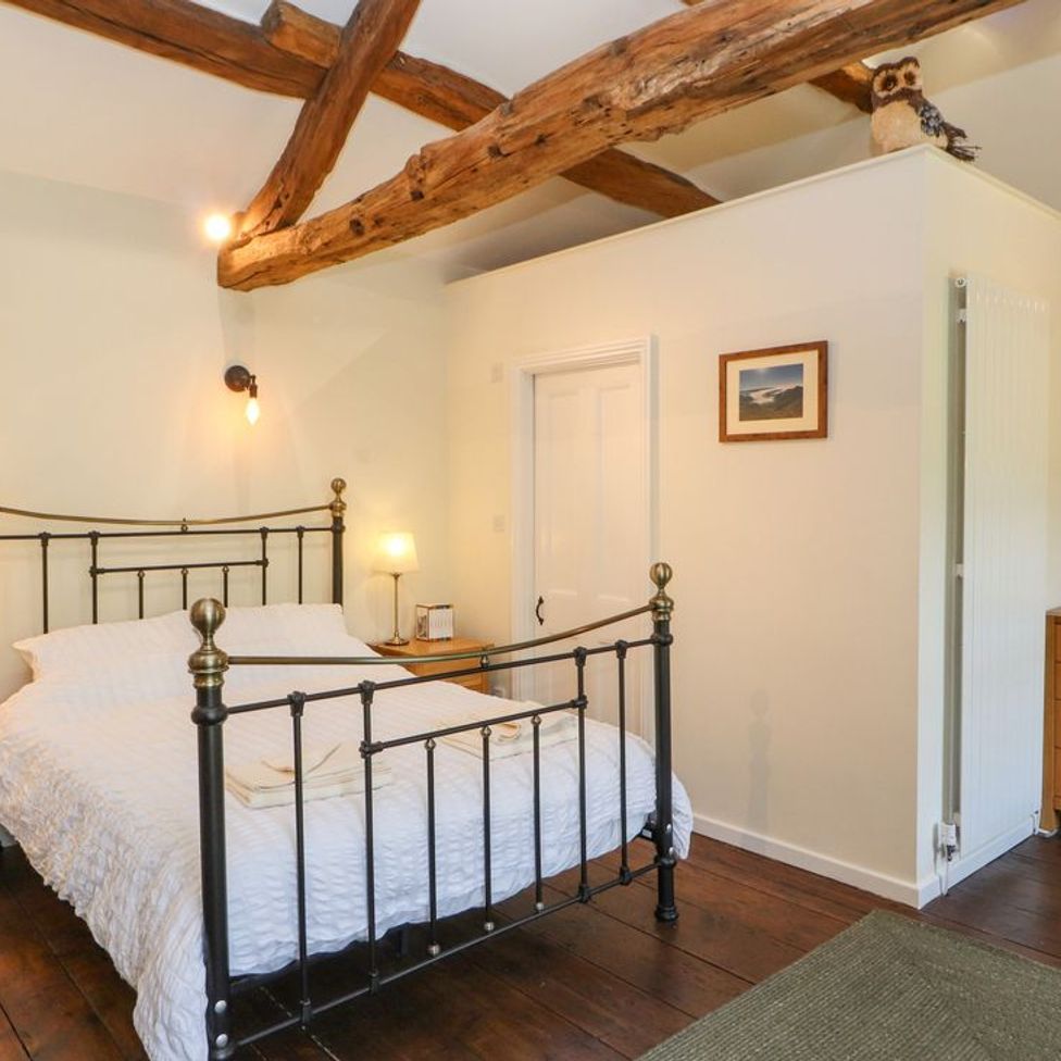 A bedroom with a metal bed frame wooden bedside tables lamps and exposed wooden ceiling beams at Roger Pot in Garsdale near Sedbergh