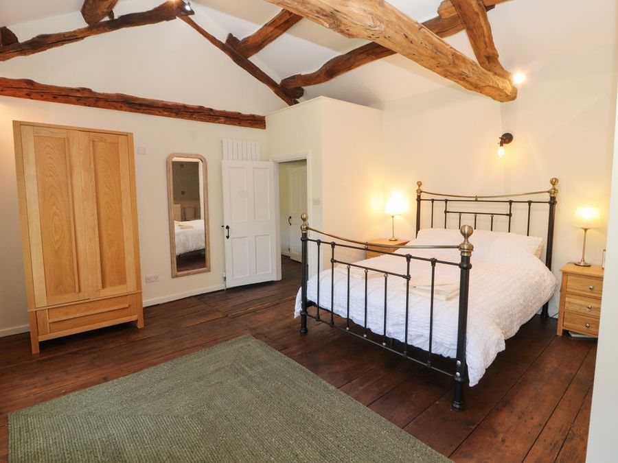 A bedroom with a metal bed frame wooden wardrobes bedside tables and exposed wooden ceiling beams at Roger Pot in Garsdale near Sedbergh