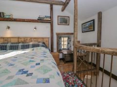 A bedroom with a wooden bed frame quilt wall shelves small window desk and wooden railing at The Old Cart House Garsdale near Sedbergh