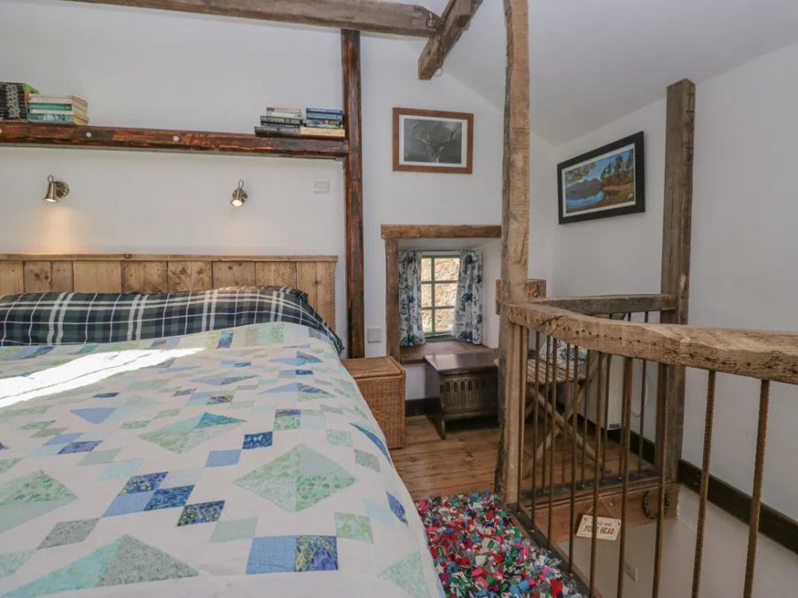 A bedroom with a wooden bed frame quilt wall shelves small window desk and wooden railing at The Old Cart House Garsdale near Sedbergh