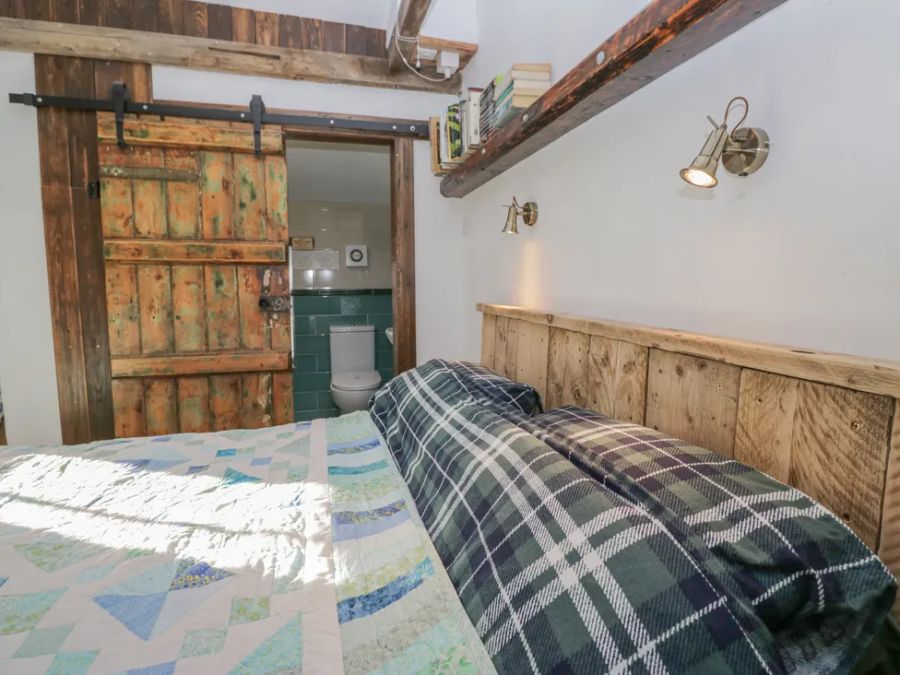 A bedroom with a wooden headboard a bed with a quilt and plaid pillows wooden sliding barn door leading to a bathroom at The Old Cart House in Garsdale near Sedbergh