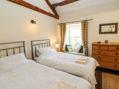 A bedroom with two single beds a wooden chest of drawers and a window seat with cushions at Roger Pot in Garsdale near Sedbergh