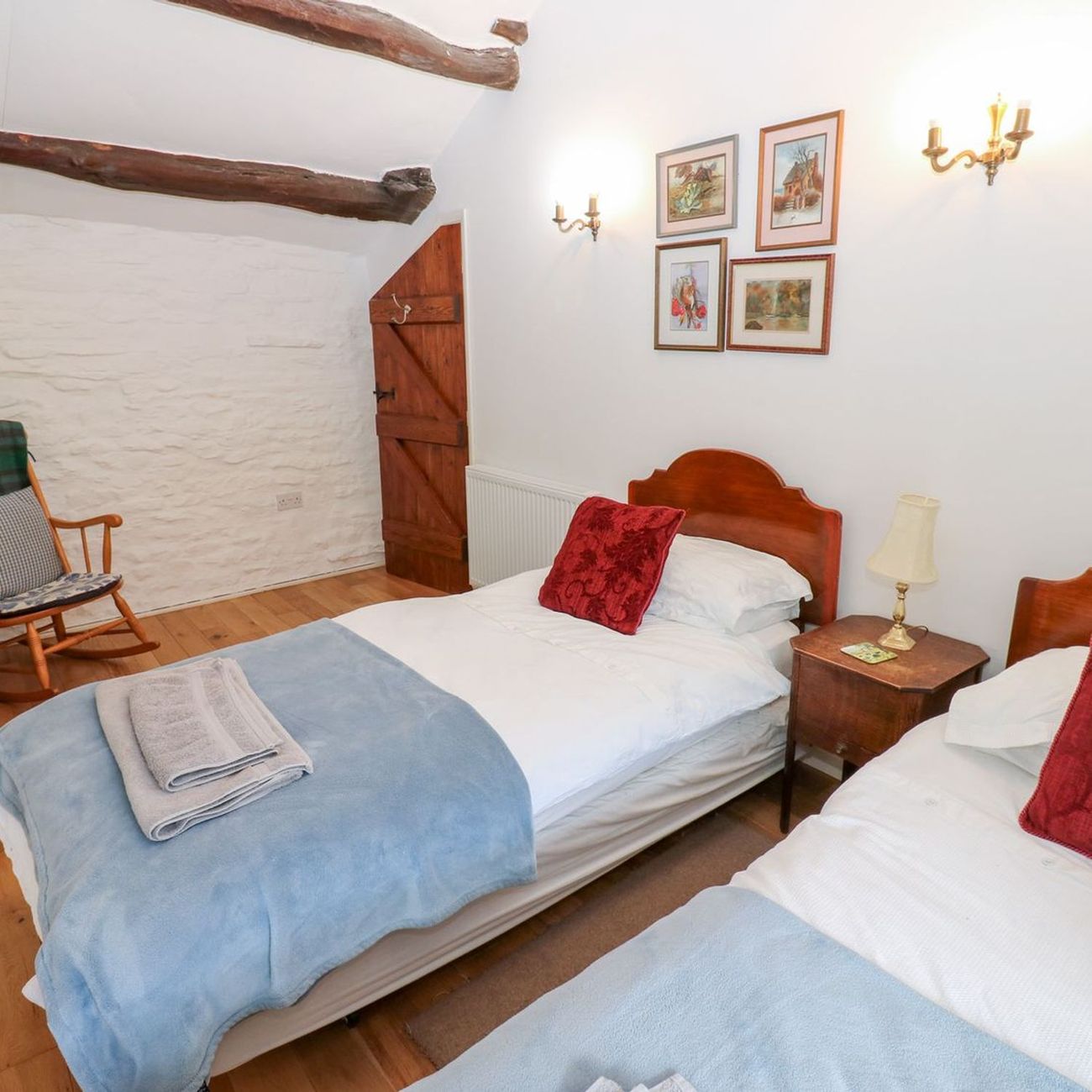 The twin bedroom at Farrier's Cottage, with two single beds, a rocking chair against the exposed stone wall and beams across the ceiling