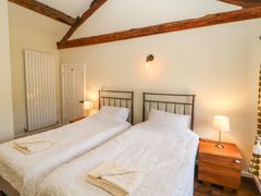 A bedroom with two single beds side by side with white bedding wooden bedside tables lamps and exposed wooden beams at Roger Pot in Garsdale near Sedbergh