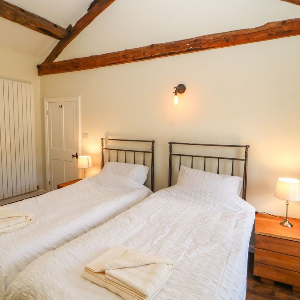 A bedroom with two single beds side by side with white bedding wooden bedside tables lamps and exposed wooden beams at Roger Pot in Garsdale near Sedbergh