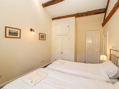 A bedroom with two single beds with white bedding towels on beds a wall light framed pictures a lamp a wardrobe and exposed wooden beams at Roger Pot in Garsdale near Sedbergh