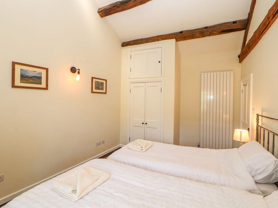 A bedroom with two single beds with white bedding towels on beds a wall light framed pictures a lamp a wardrobe and exposed wooden beams at Roger Pot in Garsdale near Sedbergh