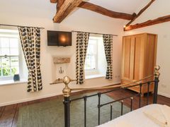 A bedroom with two windows curtains wardrobe television and exposed wooden beams at Roger Pot in Garsdale near Sedbergh