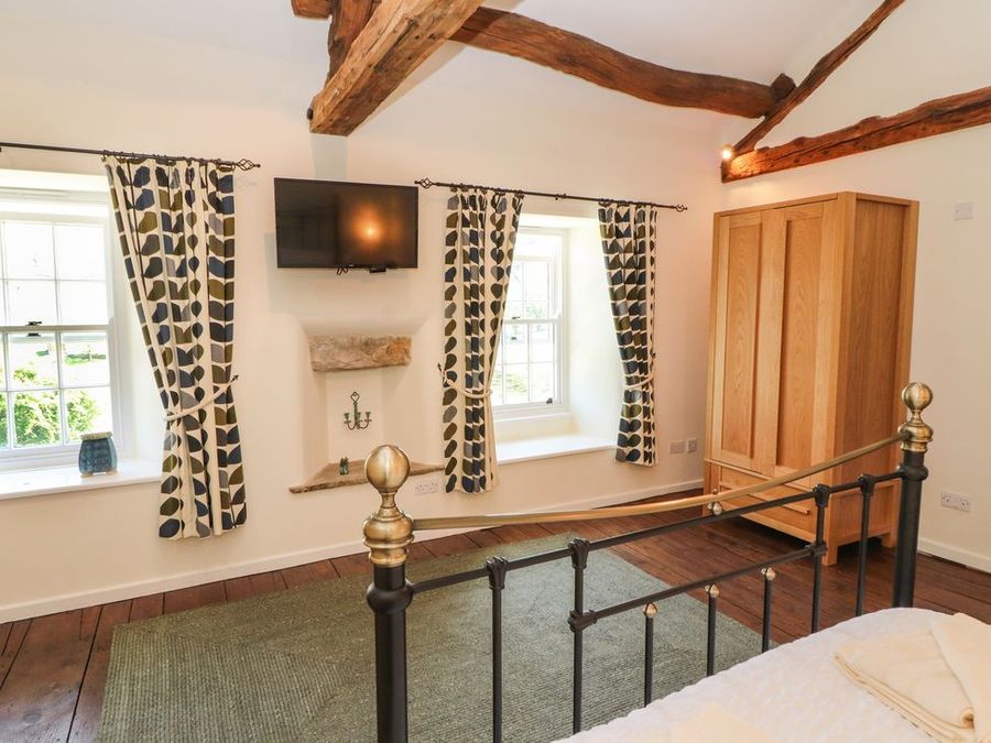 A bedroom with two windows curtains wardrobe television and exposed wooden beams at Roger Pot in Garsdale near Sedbergh