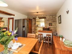 A dining area with a wooden table and chairs a flower vase and kitchen appliances in a room with stone walls at Roger Pot in Garsdale near Sedbergh