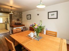 A dining room with wooden table and chairs a vase with flowers and a tray with teapot next to a stone wall opening to a kitchen at Roger Pot in Garsdale near Sedbergh