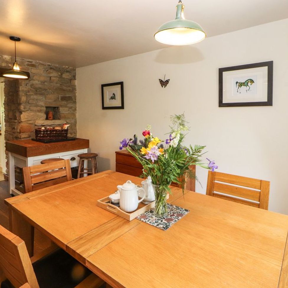 A dining room with wooden table and chairs a vase with flowers and a tray with teapot next to a stone wall opening to a kitchen at Roger Pot in Garsdale near Sedbergh