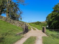 A dirt path with metal gates and stone walls surrounded by grass and trees at Roger Pot in Garsdale near Sedbergh