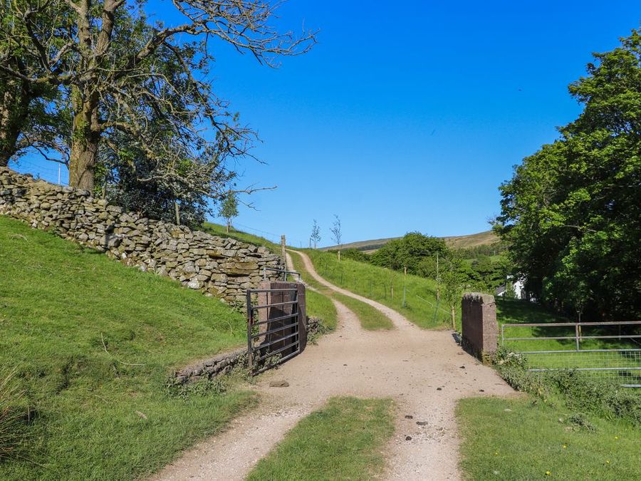 A dirt path with metal gates and stone walls surrounded by grass and trees at Roger Pot in Garsdale near Sedbergh