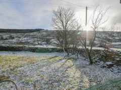 A garden with sparse snow cover trees stone walls and hills in the background at The Old Cart House in Garsdale near Sedbergh