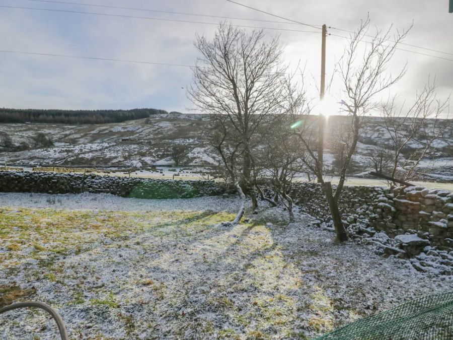 A garden with sparse snow cover trees stone walls and hills in the background at The Old Cart House in Garsdale near Sedbergh