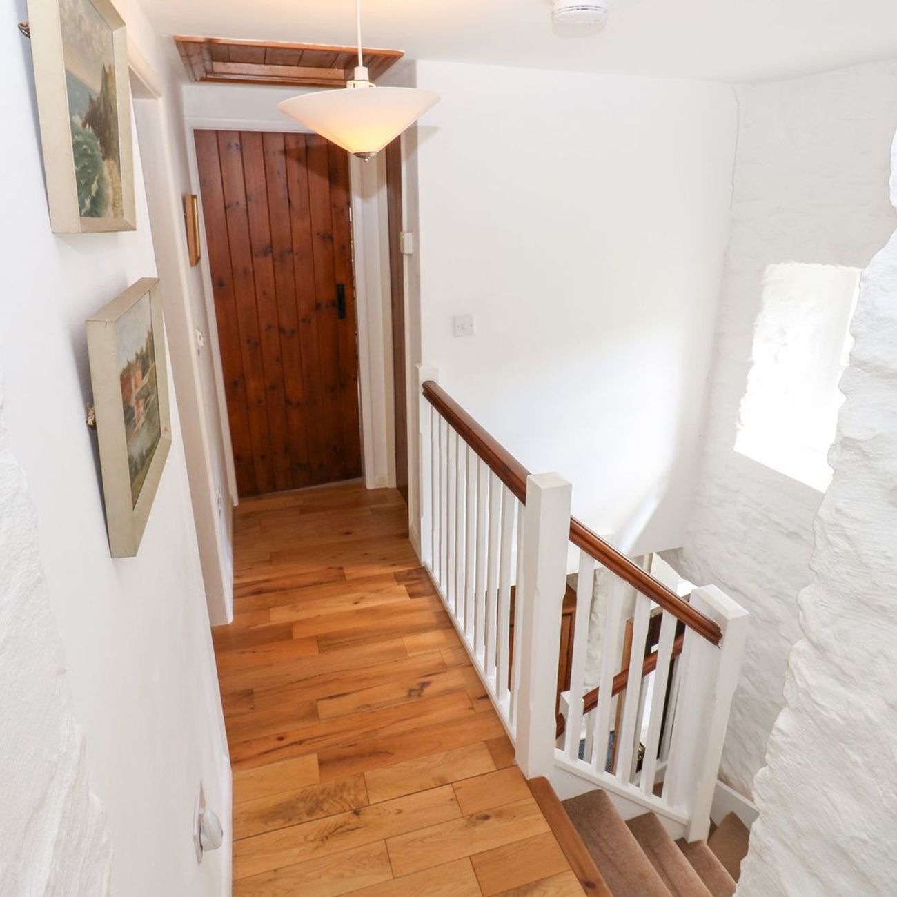 The first floor landing at Farrier's Cottage, with paintings on the whitewashed walls and the stairs dropping away to the right