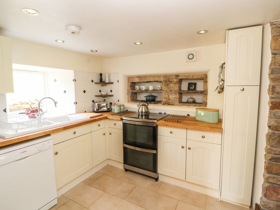 A kitchen with cream cabinets wooden countertops a stainless steel oven and tiled floor at Roger Pot in Garsdale near Sedbergh