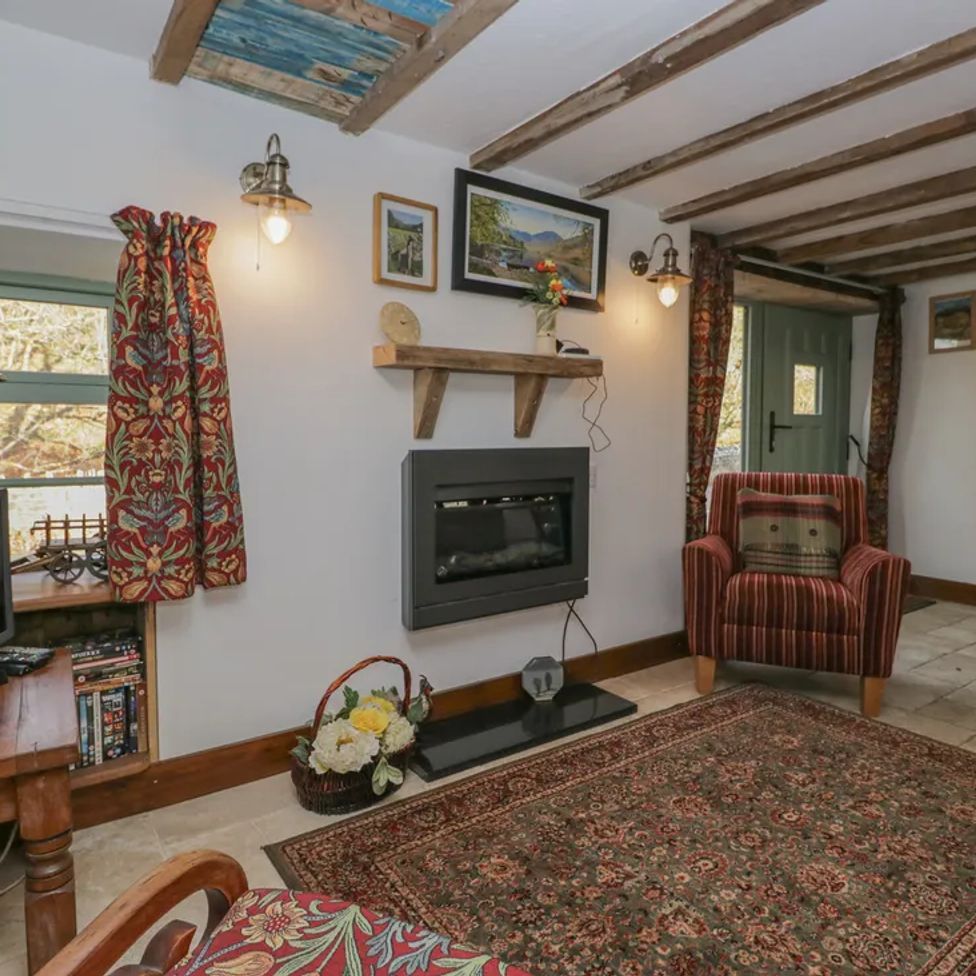 A living room with a fireplace armchair patterned curtains and a television at The Old Cart House in Garsdale near Sedbergh