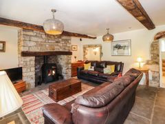 A living room with leather sofas a wood burning stove and stone walls at Roger Pot in Garsdale near Sedbergh