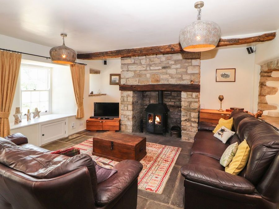 A living room with leather sofas a wooden coffee table and a stone fireplace at Roger Pot in Garsdale near Sedbergh