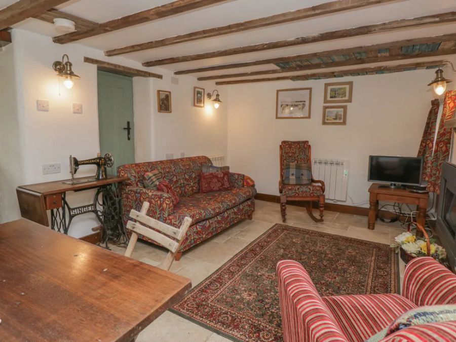 A living room with patterned sofas a wooden table a vintage sewing machine and a TV at The Old Cart House in Garsdale near Sedbergh