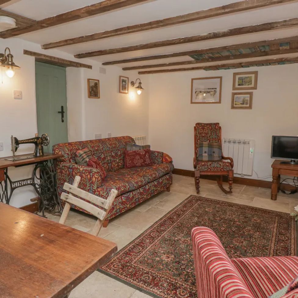 A living room with patterned sofas a wooden table a vintage sewing machine and a TV at The Old Cart House in Garsdale near Sedbergh
