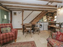 A living room with striped and floral armchairs a wooden table and chairs under stairs with washing machine and vintage sewing machine at The Old Cart House in Garsdale near Sedbergh