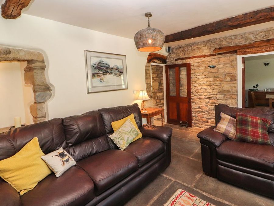 A living room with two leather sofas cushions a wooden side table lamp and exposed stone walls at Roger Pot in Garsdale near Sedbergh