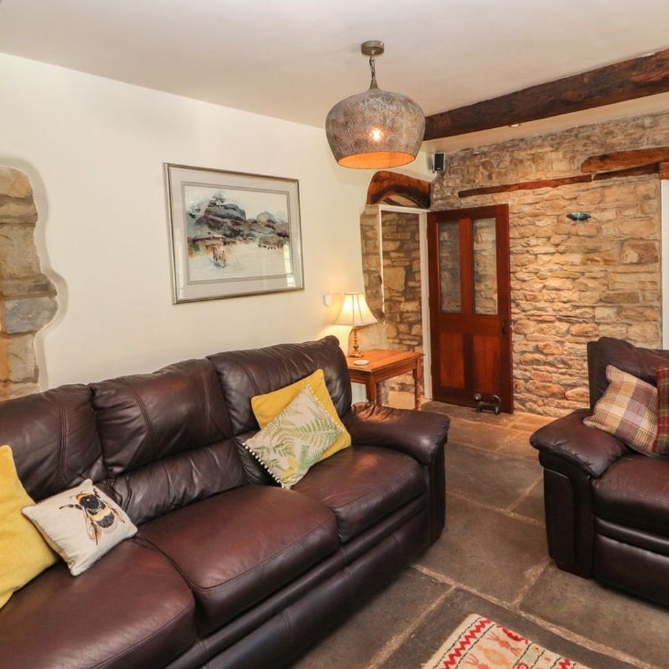 A living room with two leather sofas cushions a wooden side table lamp and exposed stone walls at Roger Pot in Garsdale near Sedbergh