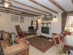 A living room with wooden beams floral and striped chairs a rug a sewing machine and a TV at The Old Cart House in Garsdale near Sedbergh
