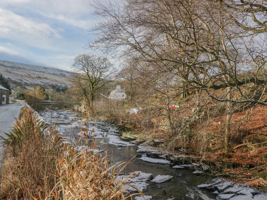 A river flowing alongside a road with leafless trees and a house in the background at The Old Cart House in Garsdale near Sedbergh