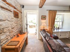 A room with a leather sofa near a window with curtains and a wooden console table against a stone wall at Roger Pot in Garsdale near Sedbergh