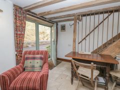 A room with a red striped armchair near an open door and wooden table with chairs under a staircase at The Old Cart House in Garsdale near Sedbergh