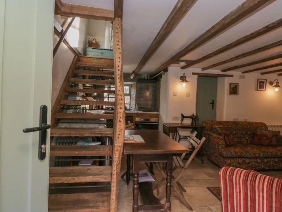 A rustic living area with wooden staircase, dining table with chairs, floral sofa, and vintage sewing machine at The Old Cart House in Garsdale near Sedbergh