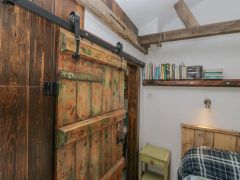 A rustic sliding wooden door next to a small bedside table and a shelf with books in a bedroom at The Old Cart House in Garsdale near Sedbergh