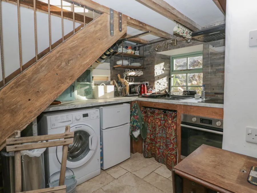 A small kitchen with a washing machine fridge oven wooden stairs and window at The Old Cart House in Garsdale near Sedbergh