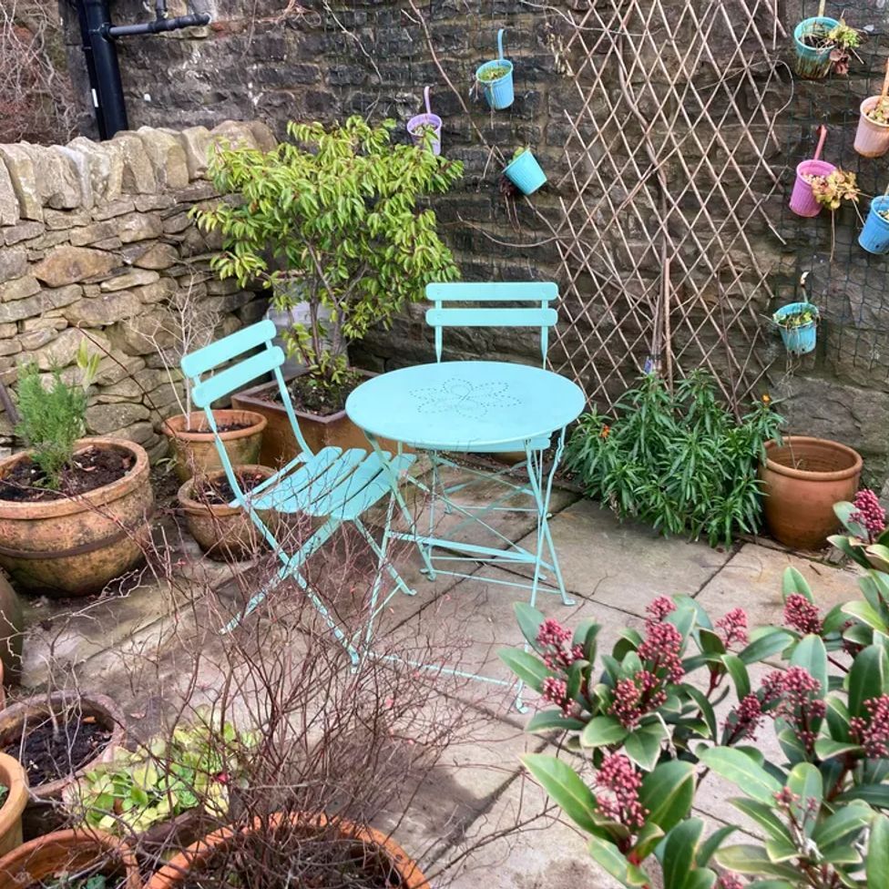 A small outdoor patio with a blue metal table and two chairs surrounded by potted plants at The Old Cart House in Garsdale near Sedbergh