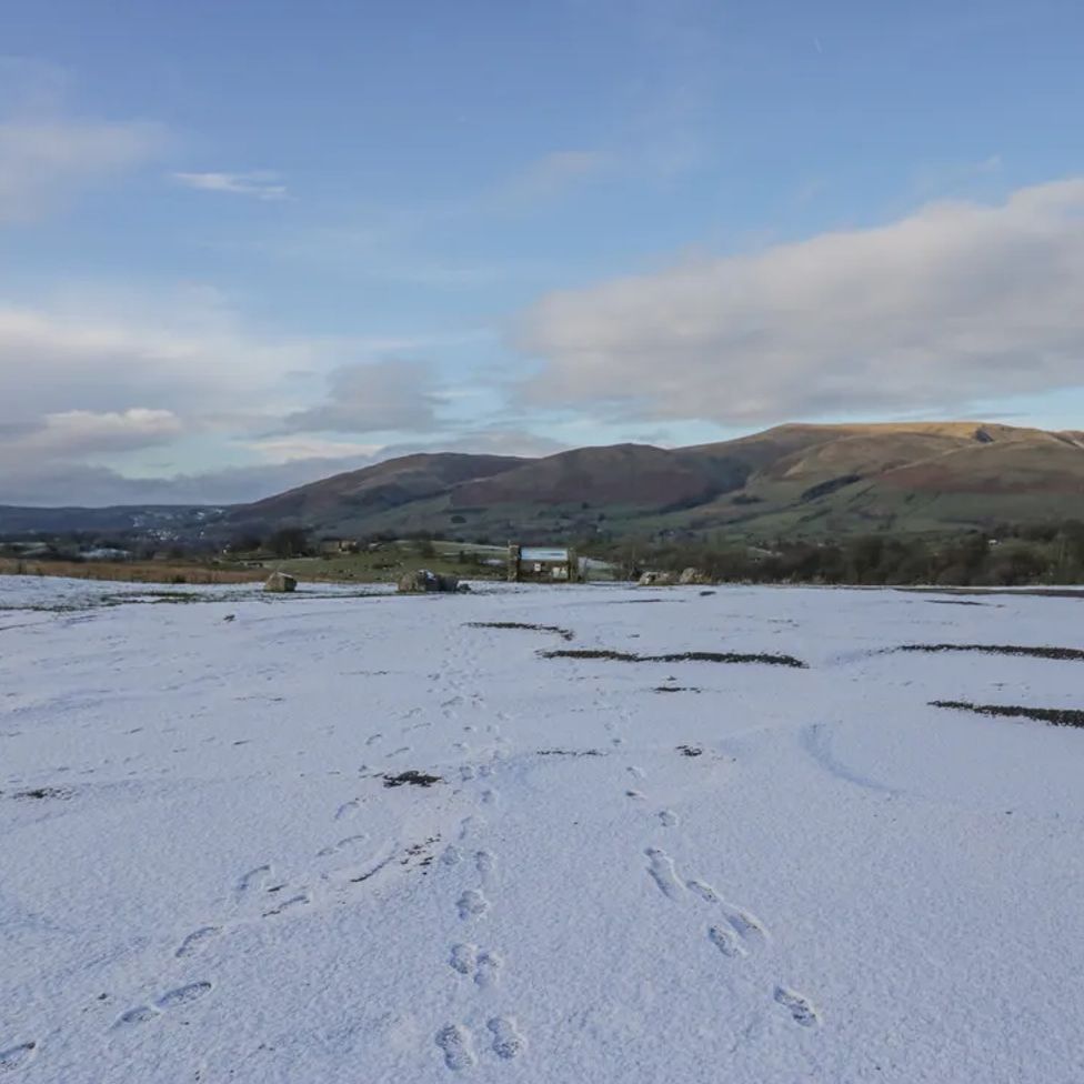 A snowy field with footprints leading to a gate and hills in the background at The Old Cart House in Garsdale near Sedbergh