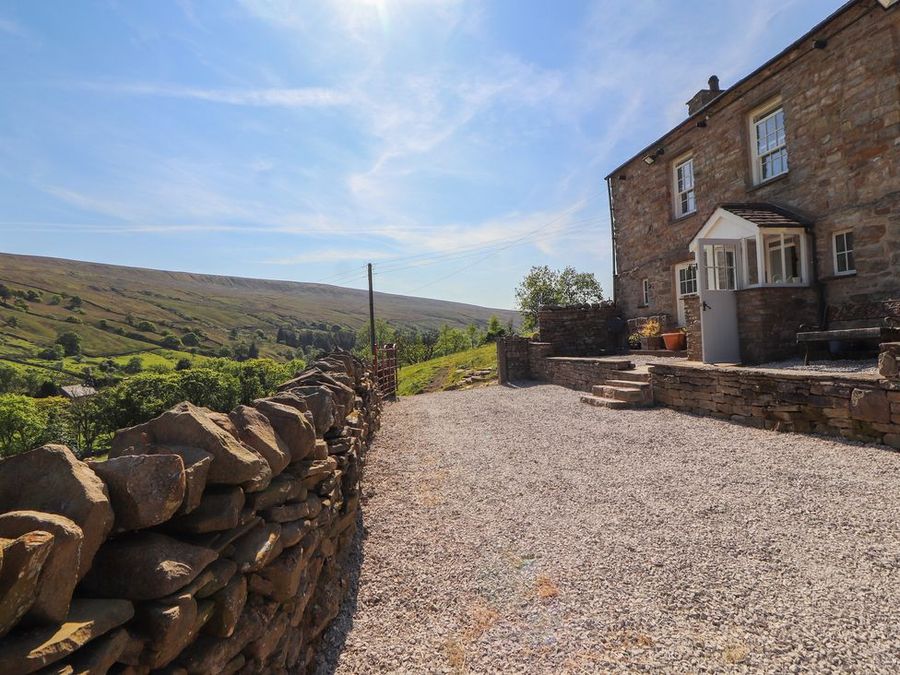 A stone cottage with gravel driveway and dry stone wall overlooking green hills at Roger Pot in Garsdale near Sedbergh