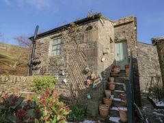 A stone house with a staircase lined with plant pots and a green door at The Old Cart House in Garsdale near Sedbergh