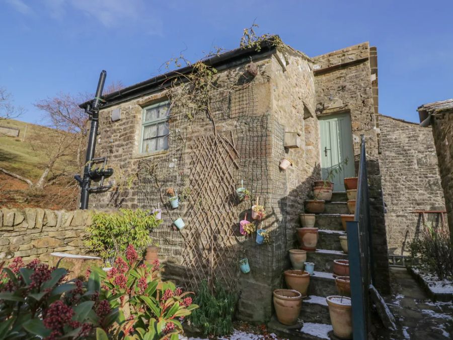 A stone house with a staircase lined with plant pots and a green door at The Old Cart House in Garsdale near Sedbergh
