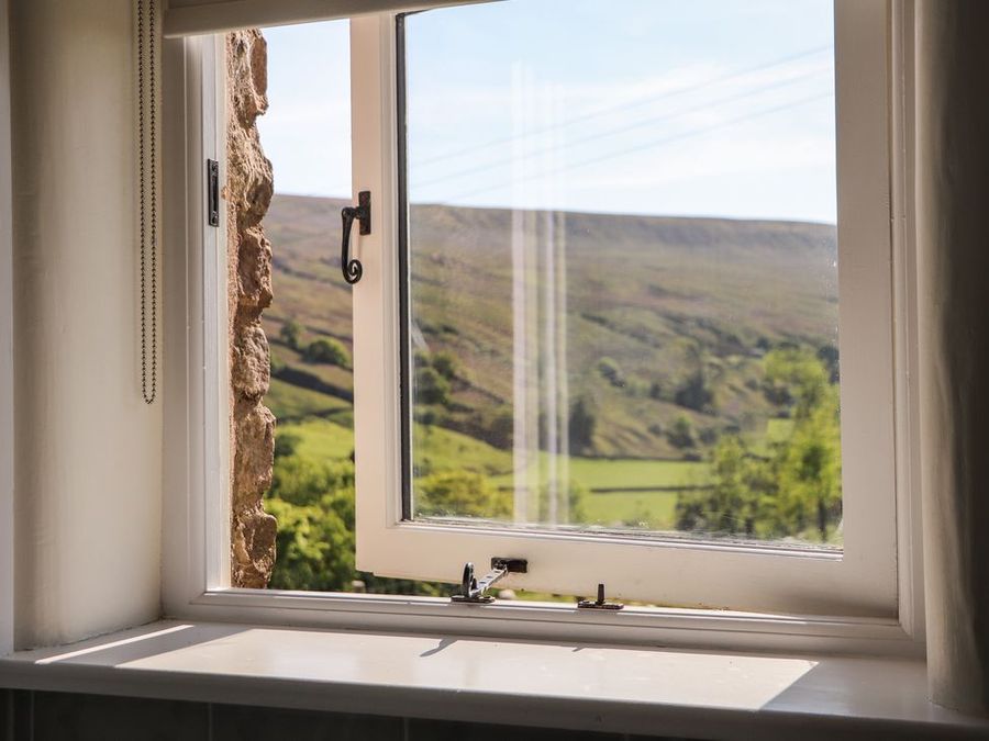 An open window with a latch and stone wall visible with hills and green fields outside at Roger Pot in Garsdale near Sedbergh